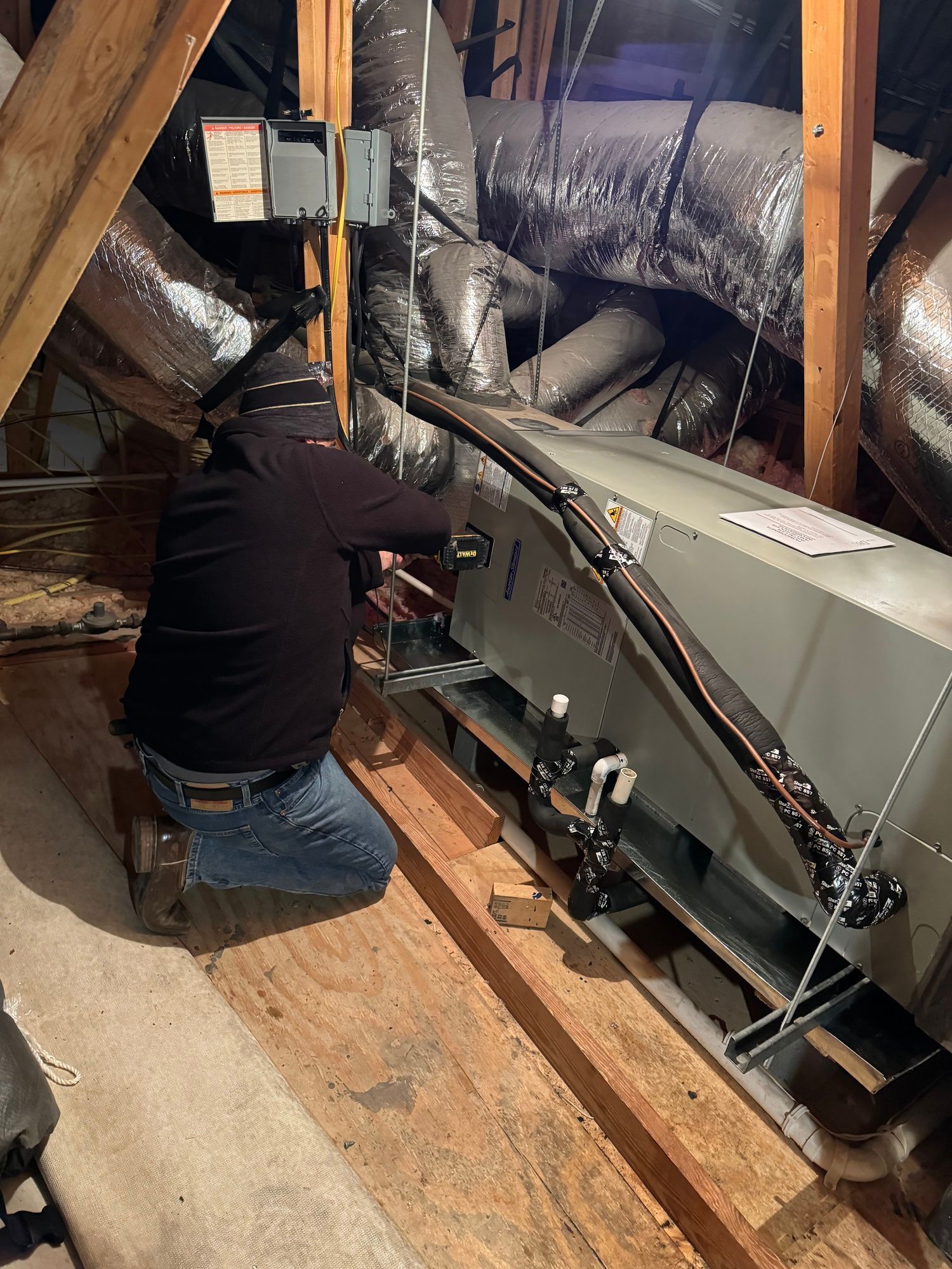 A man is kneeling down in an attic working on a machine.