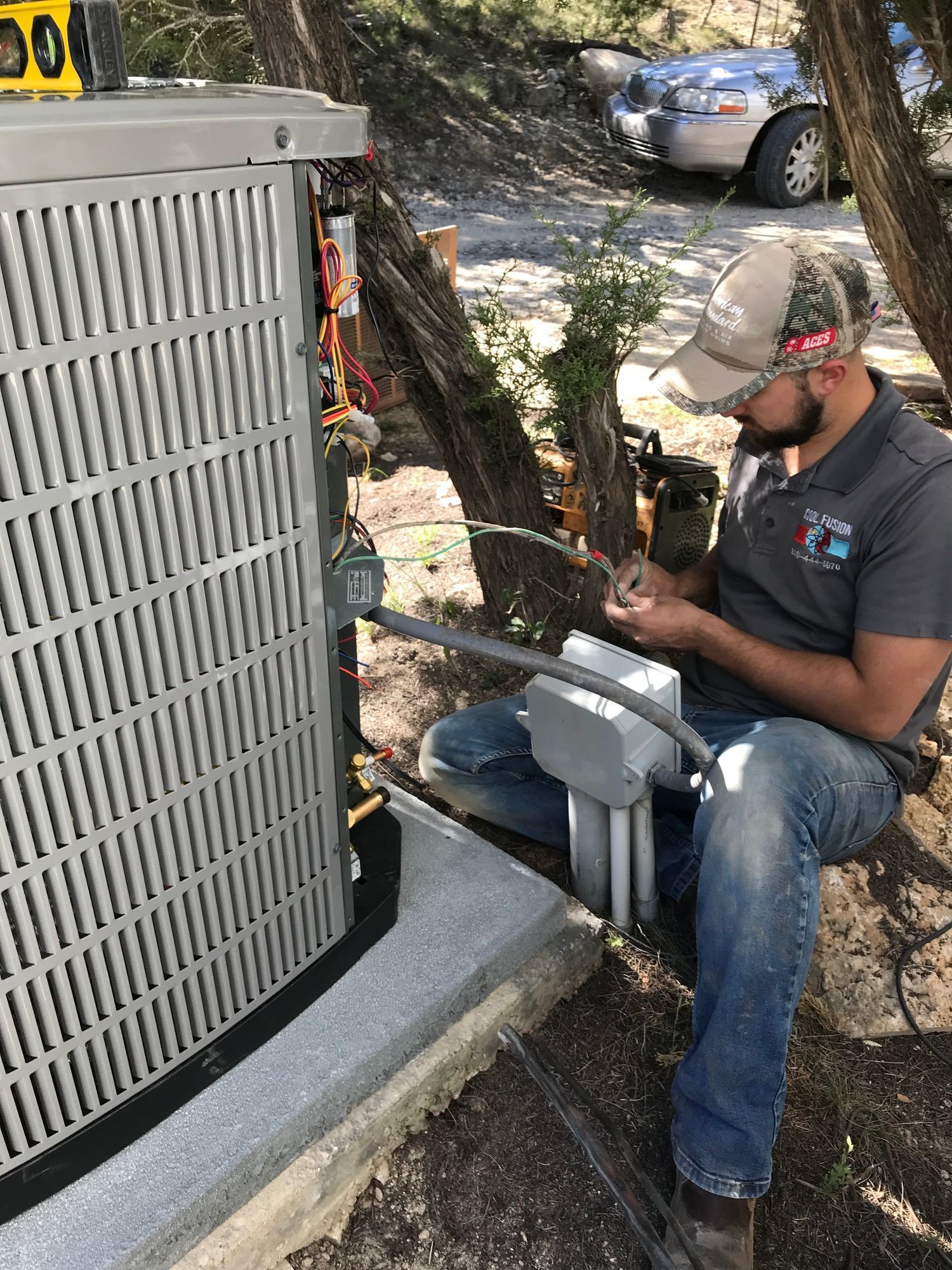 A man is sitting on the ground working on an air conditioner.