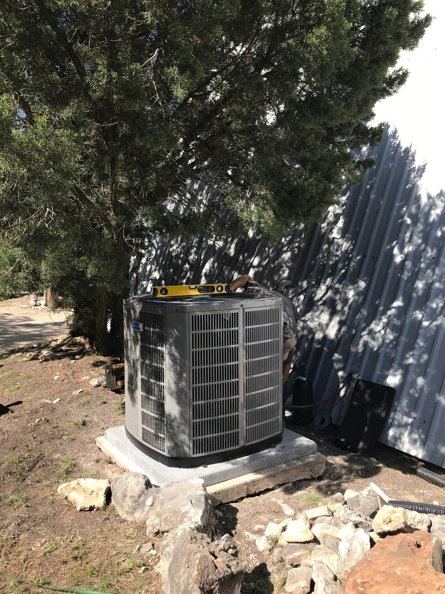 A large air conditioner is sitting under a tree in a yard.