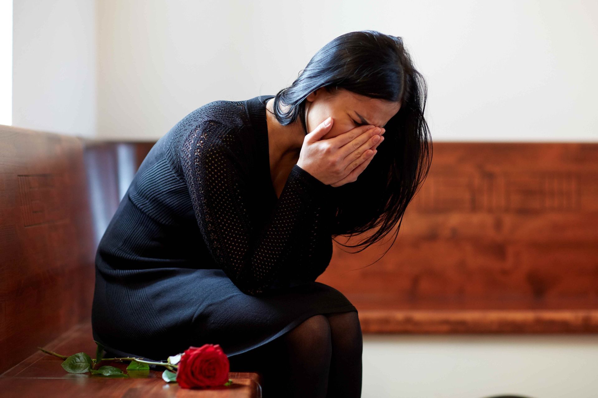 A woman is sitting on a bench with a red rose and crying