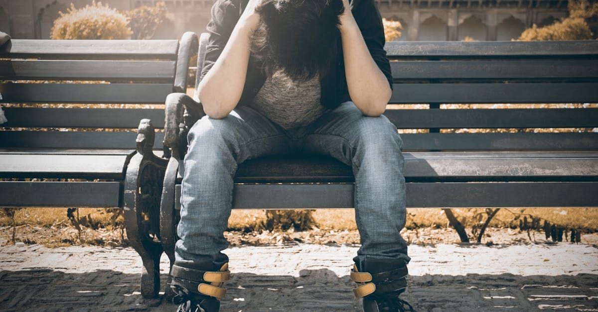 A person is sitting on a park bench with their head in their hands.