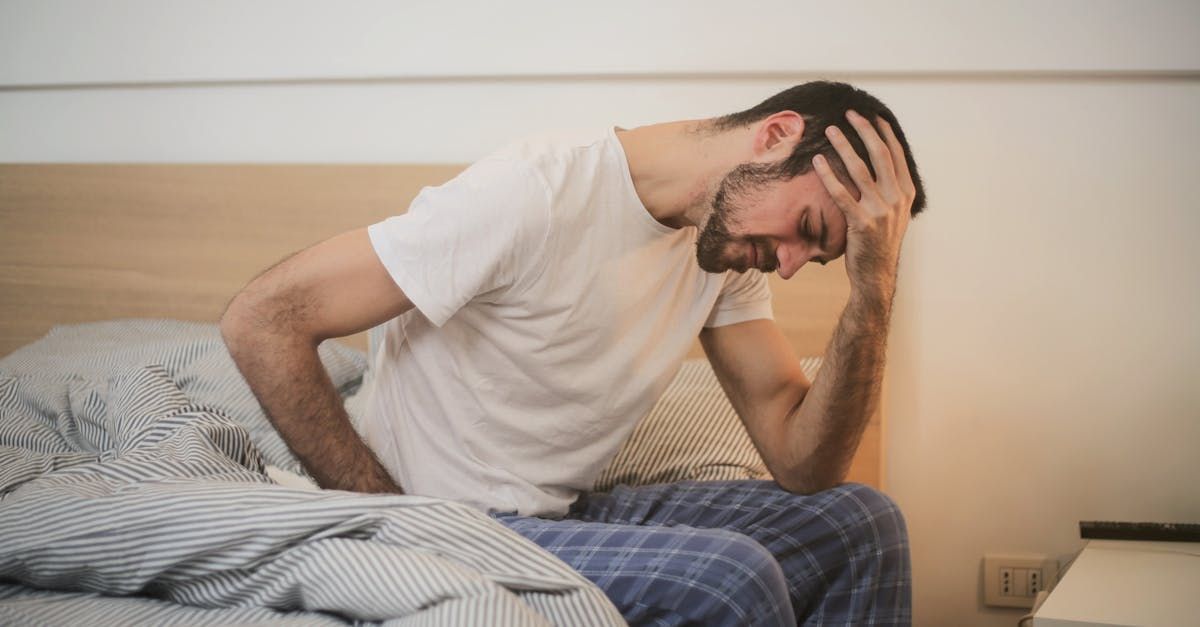 A man is sitting on a bed with his hand on his head.