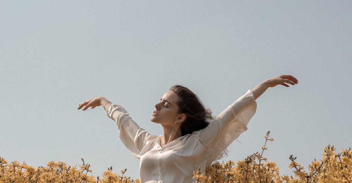 A woman is standing in a field of flowers with her arms outstretched.