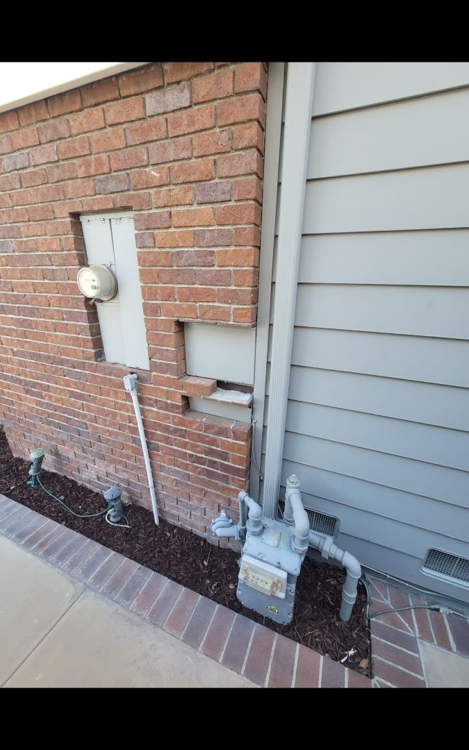Exterior view of a brick wall and light gray siding with a gas meter and electric meter.