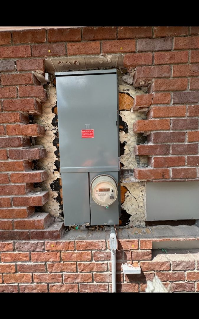 Metal electrical box and meter recessed into a brick wall.