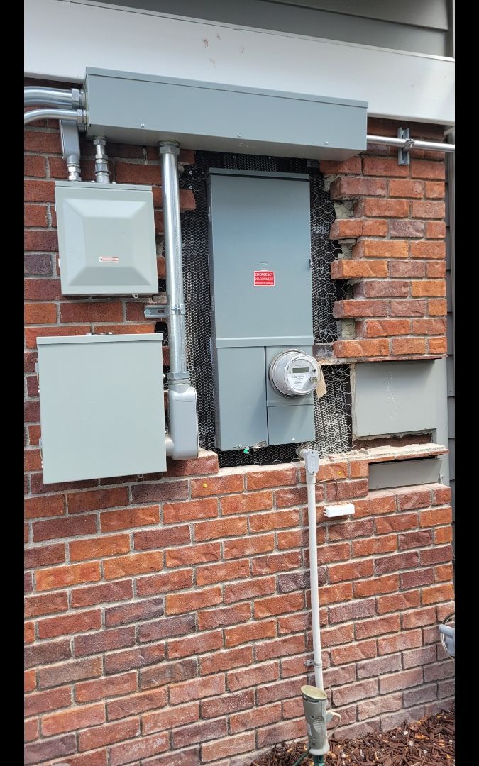 Electrical boxes and conduit mounted on a brick wall. Gray boxes, wires, and conduit.