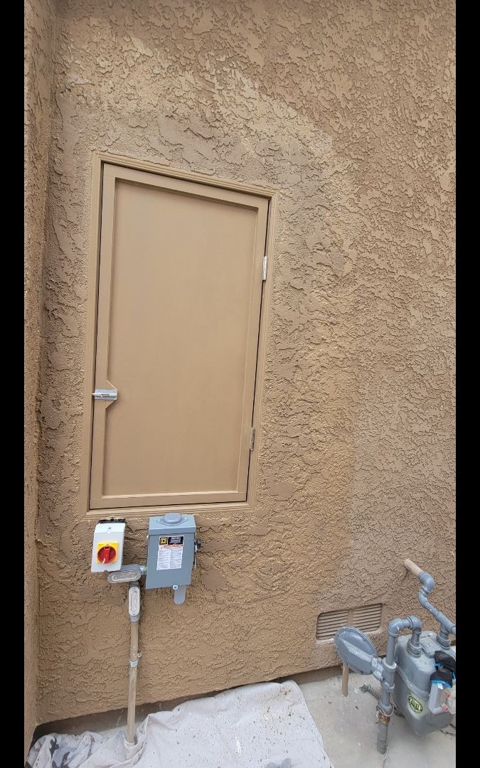 Tan door with a metal frame in a textured tan wall, with electrical boxes and gas meters below.