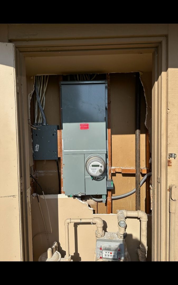 Electrical meter and panel in recessed outdoor enclosure; wires and conduit visible.