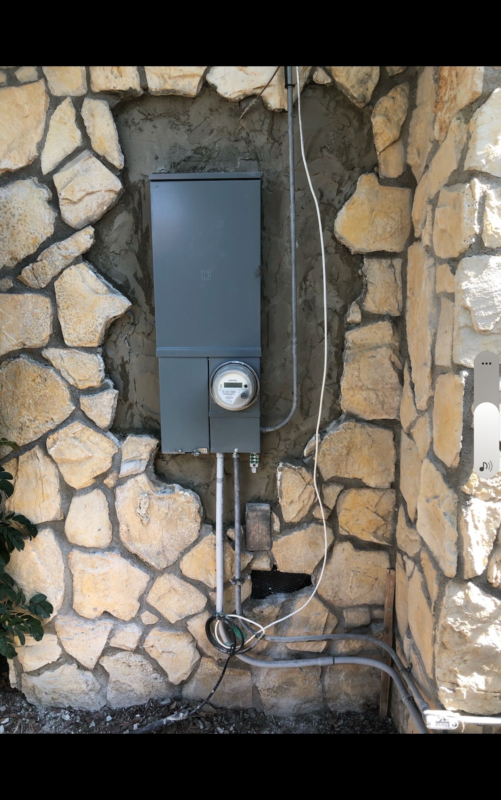 Electric meter box mounted in a stone wall, with conduit and wires.