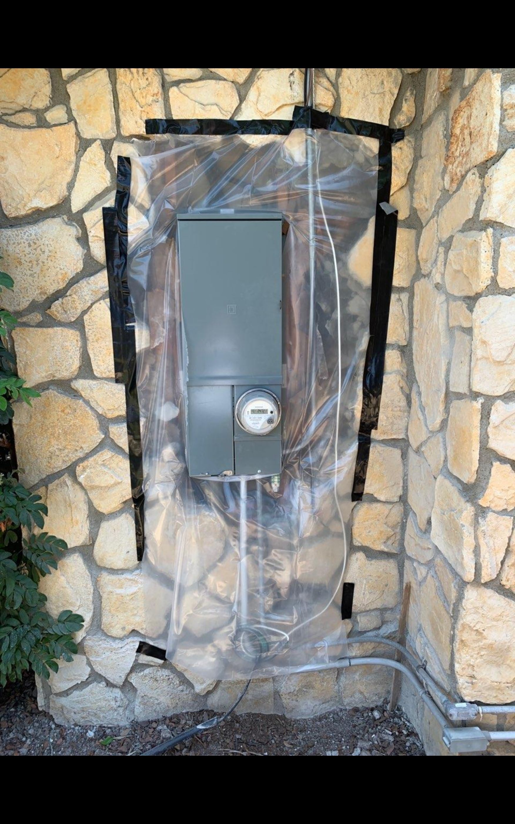 Electrical panel installed on a stone wall, covered in plastic sheeting.