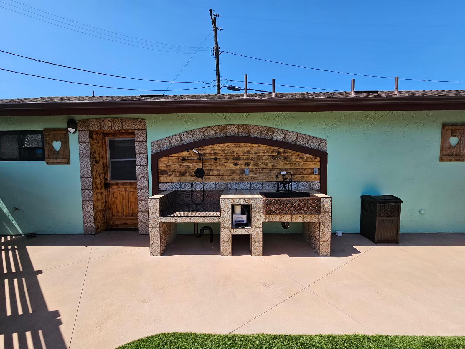 Outdoor kitchen with brick and stone features, teal wall, and concrete patio.