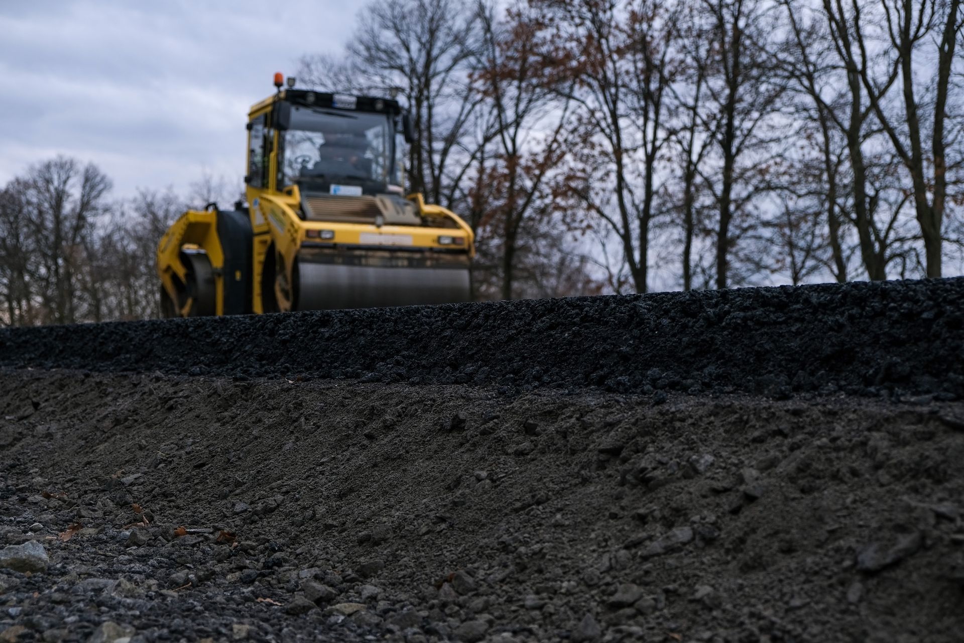 Yellow road roller compacting fresh asphalt on a new road.