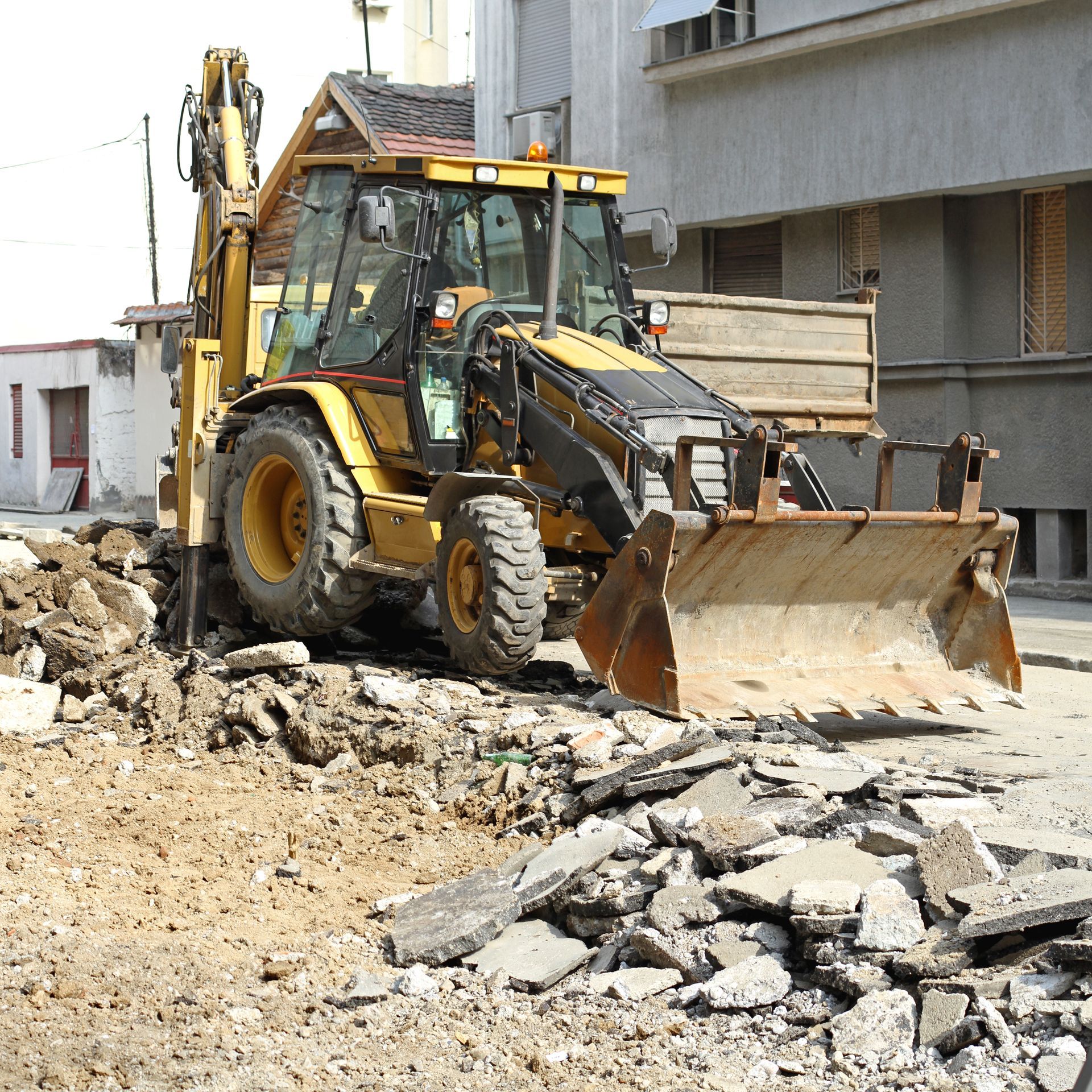 Yellow backhoe operating on a construction site, removing debris.