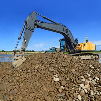 Excavator with raised bucket, moving soil, outdoors, under a blue sky.