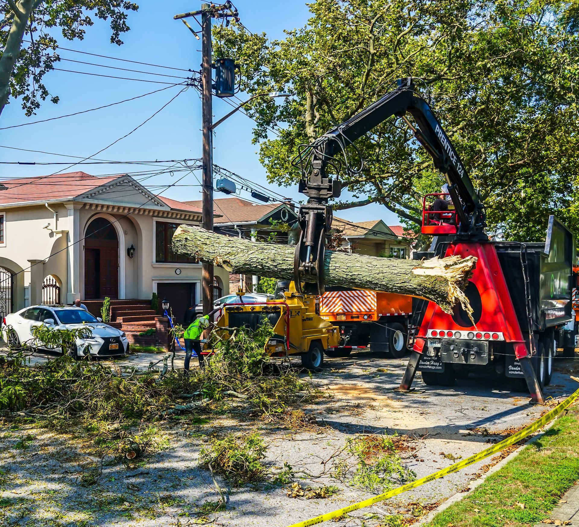 Tree branches being fed into a wood chipper on a residential street. Workers and utility truck in the background.
