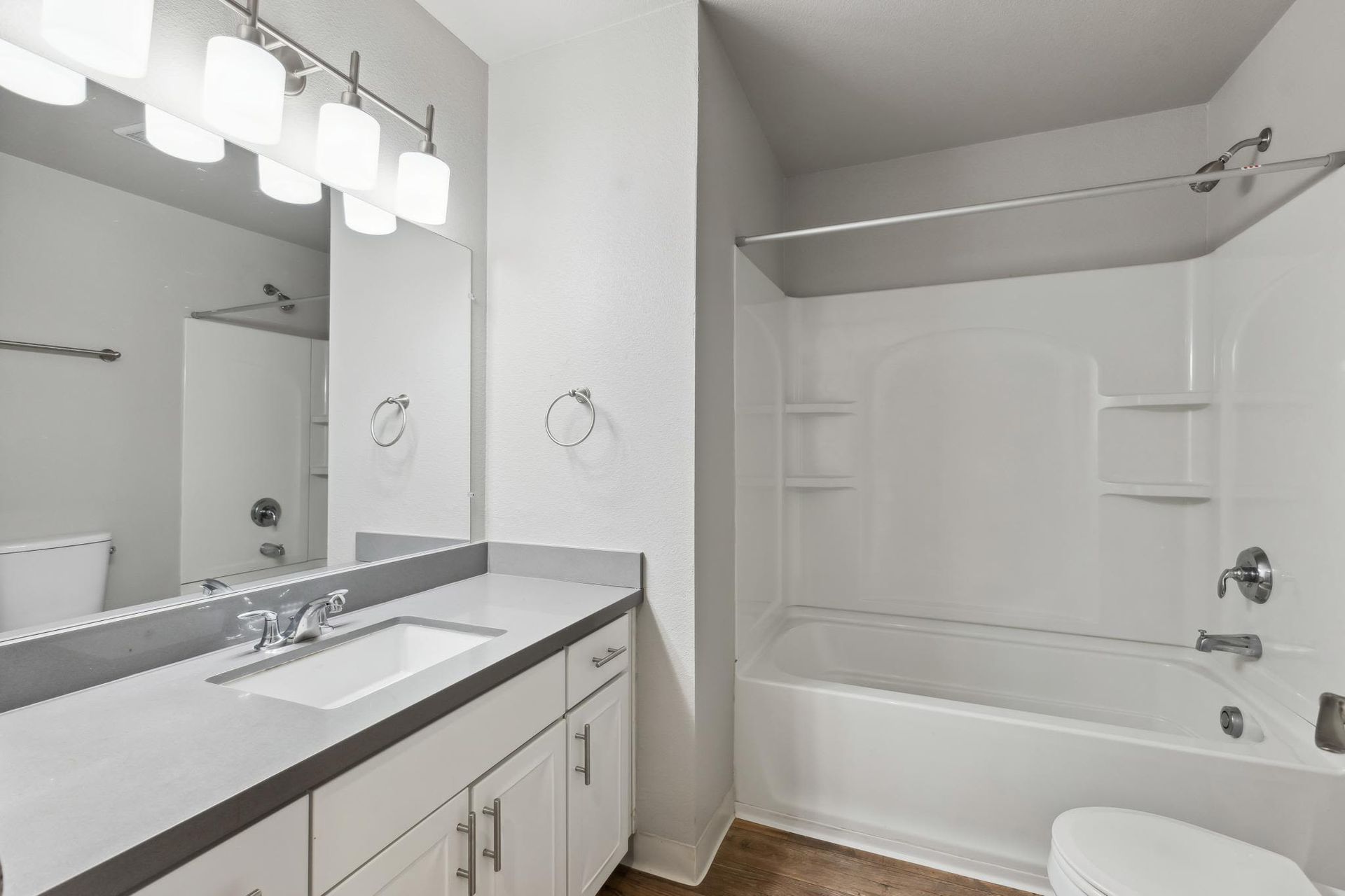 White bathroom with a single vanity, large mirror, and a bathtub/shower combo.