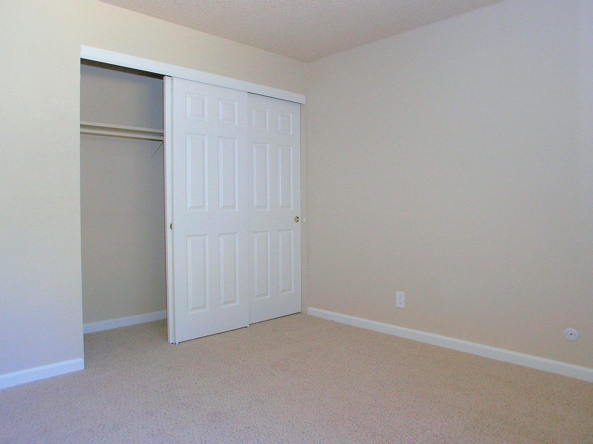 Empty bedroom with beige walls, light carpet, and a white sliding closet door.
