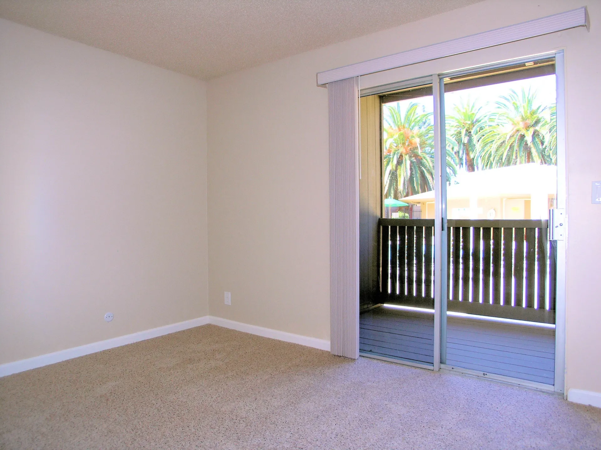 Beige interior room with a sliding glass door opening to a balcony and palm trees outside.