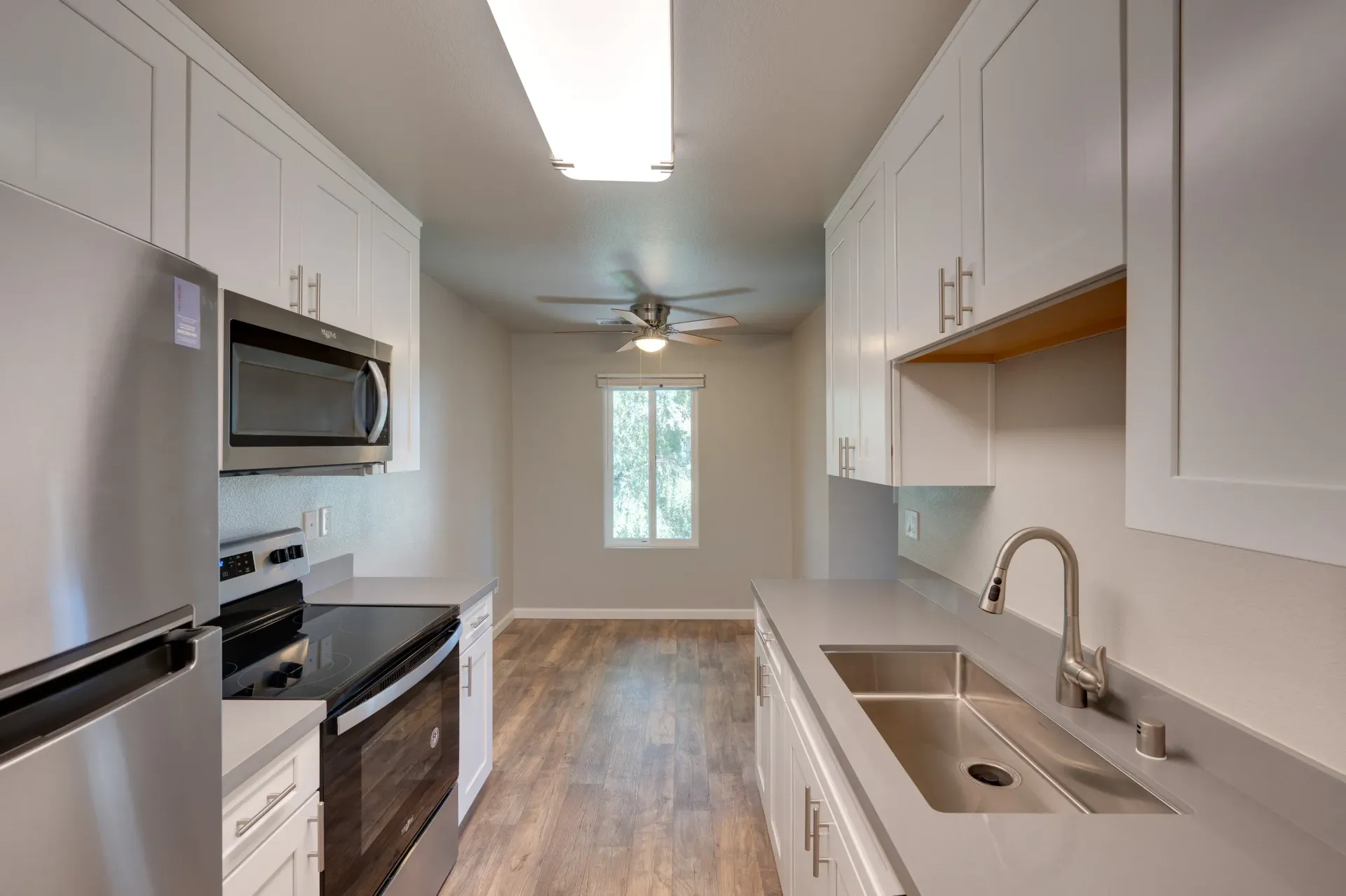 Modern galley kitchen with white cabinets, stainless steel appliances, and a double sink.