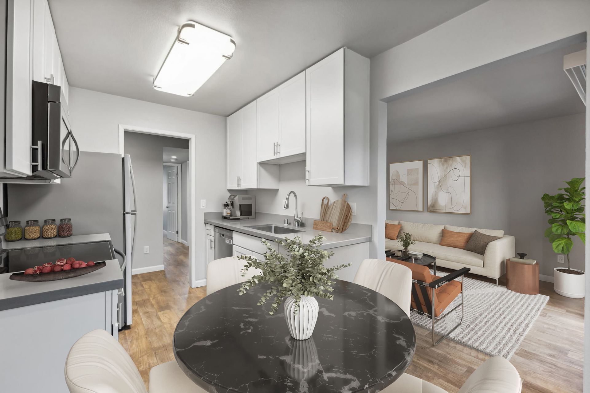 Open-concept kitchen with white cabinets and a round black marble dining table; living area visible.