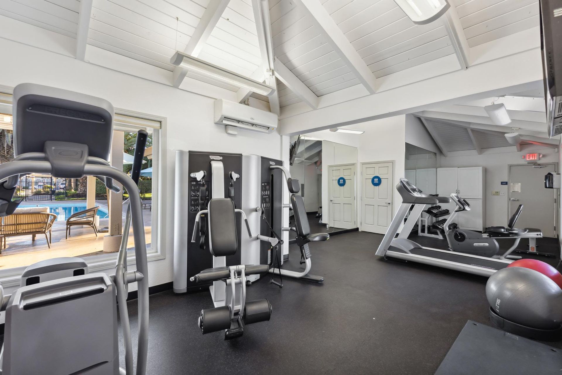 Indoor fitness center with treadmills, weight machines, and a view of the pool outside.