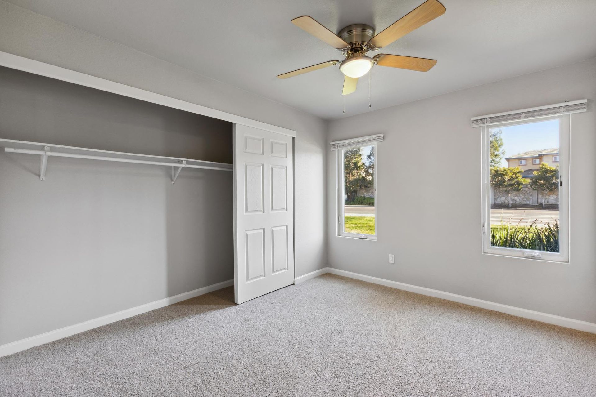 Bedroom with built-in closet, two windows, ceiling fan, and beige carpet.