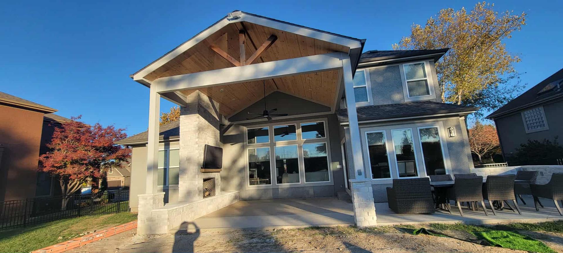 Custom Porches A two-story house with a covered patio and large windows. The sky is blue and the grass is green.