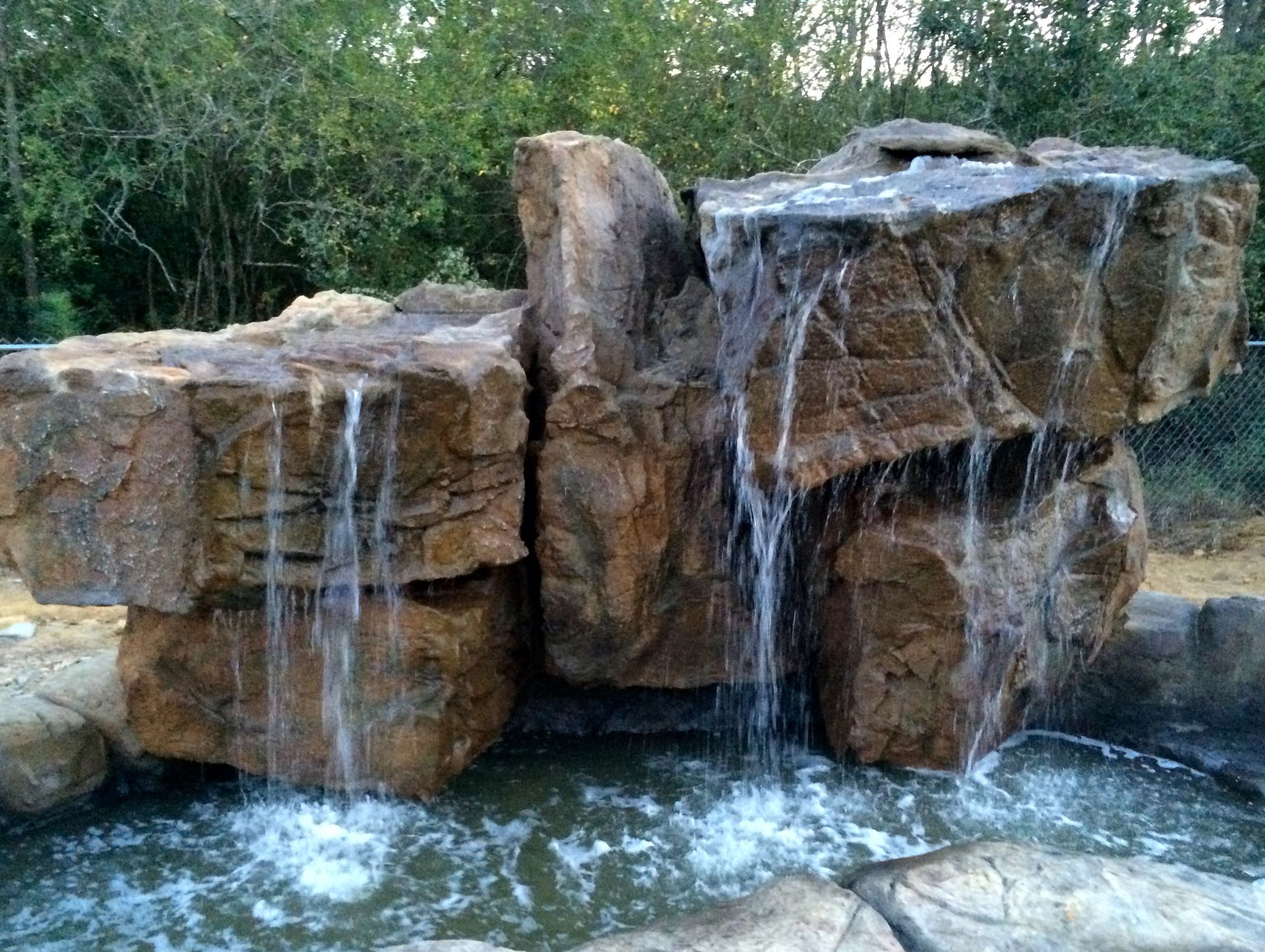 A waterfall is surrounded by rocks and trees in a park.