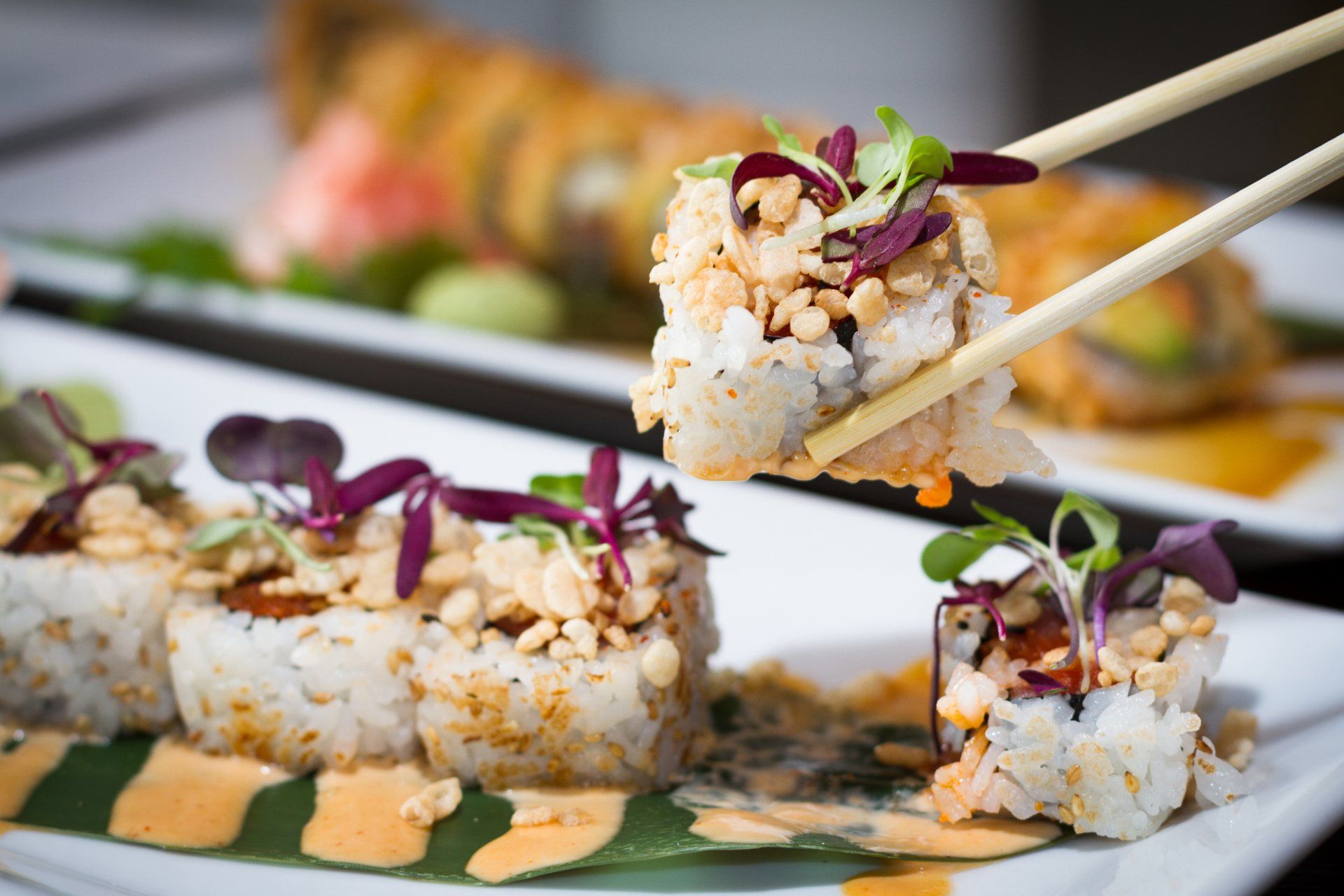 a person is holding a piece of sushi with chopsticks .