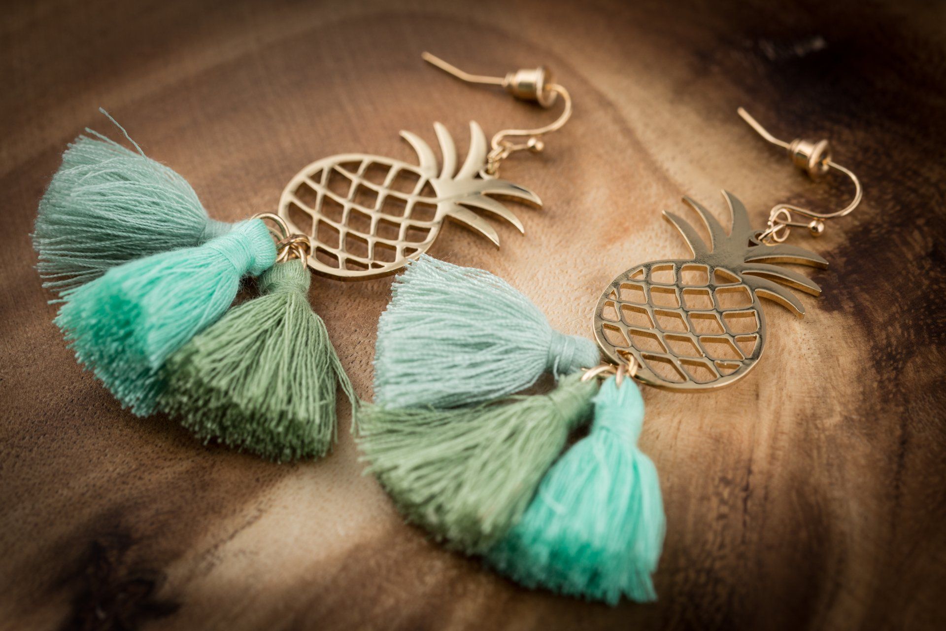 a pair of pineapple earrings with tassels on a wooden table .