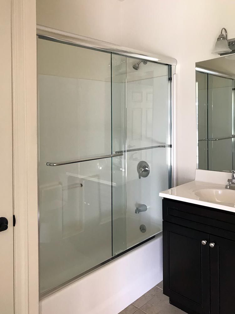 Shower with glass doors next to a bathroom vanity. Black cabinet with a white countertop.