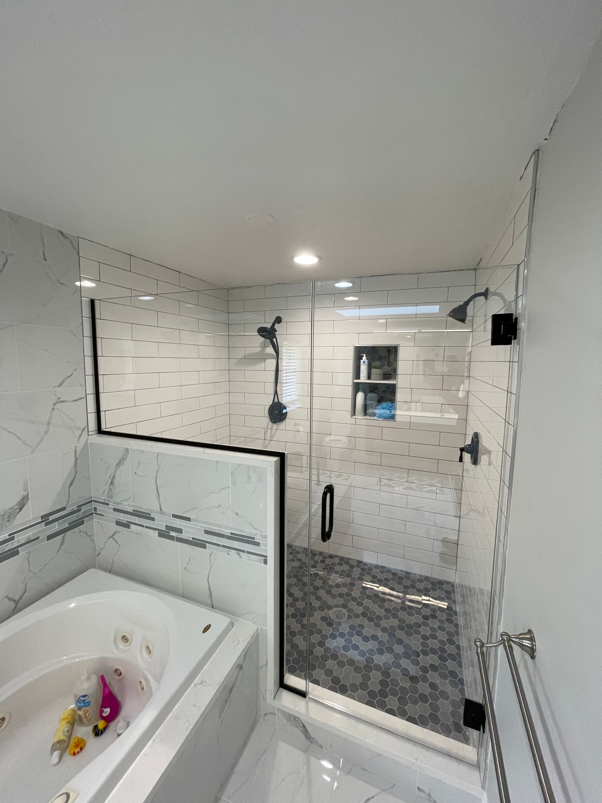 Bathroom with white marble tiles, a glass shower, a tub, and black fixtures.