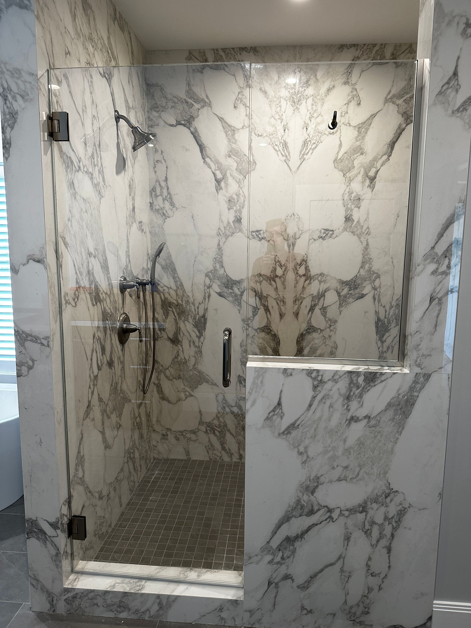 Marble-tiled shower with glass doors and chrome fixtures.