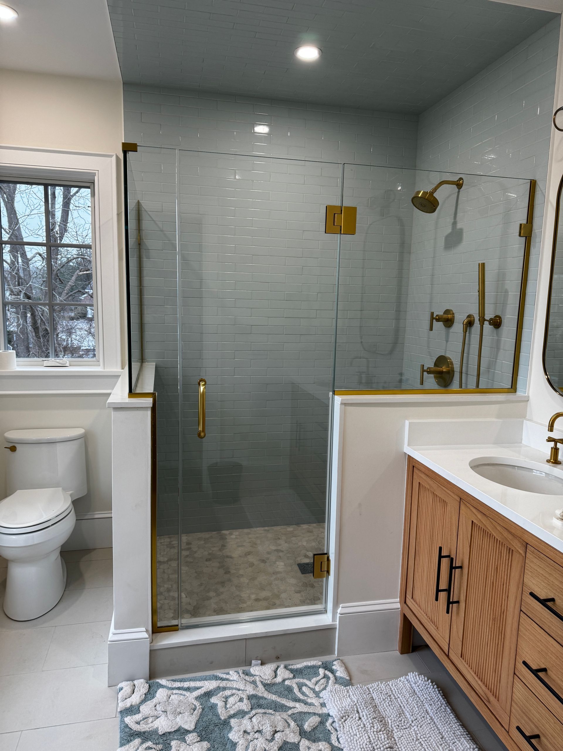 Bathroom with a glass shower, gold fixtures, wooden vanity, and a white toilet.