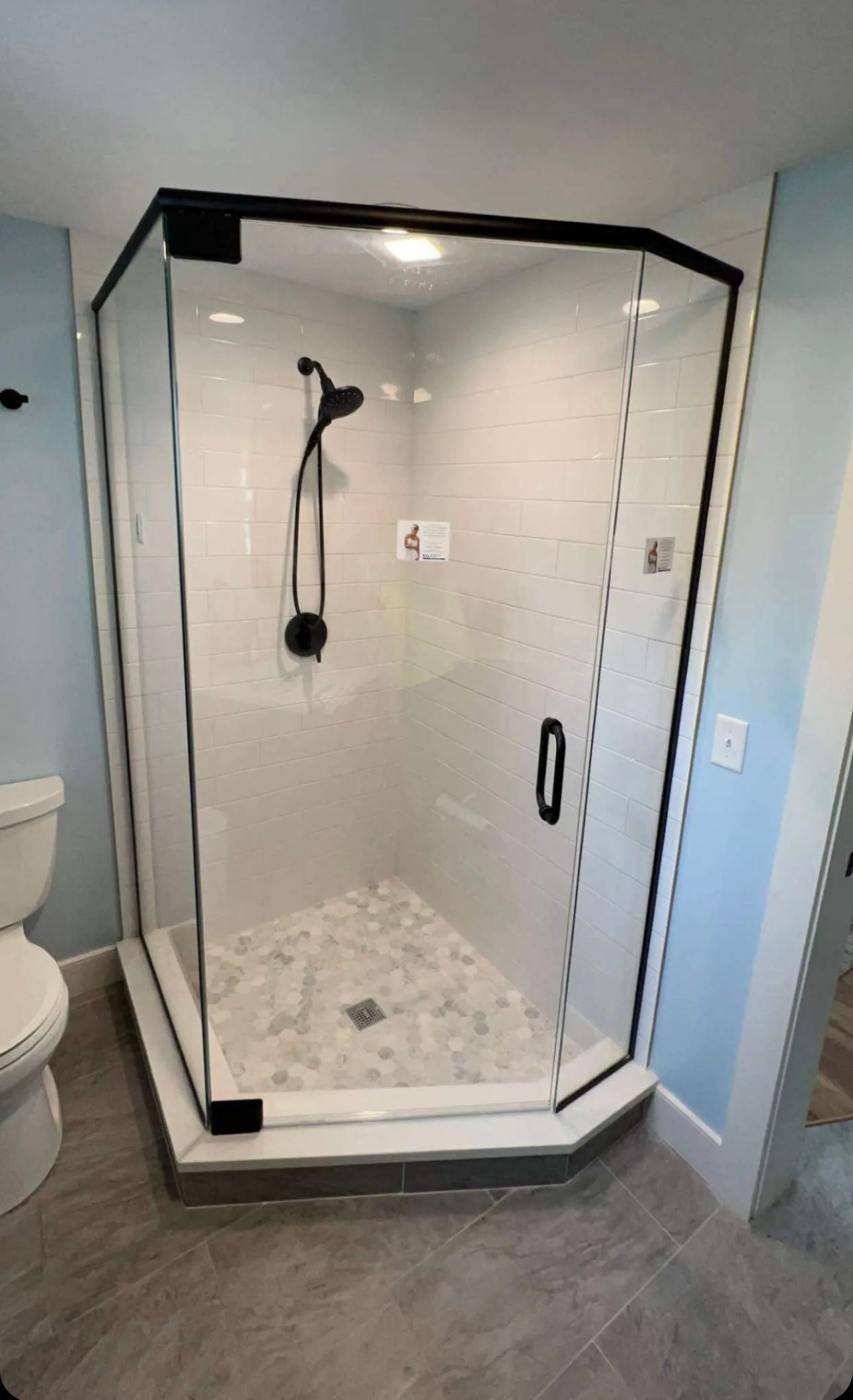 Modern glass shower enclosure with black trim, white tile walls, and pebble floor.