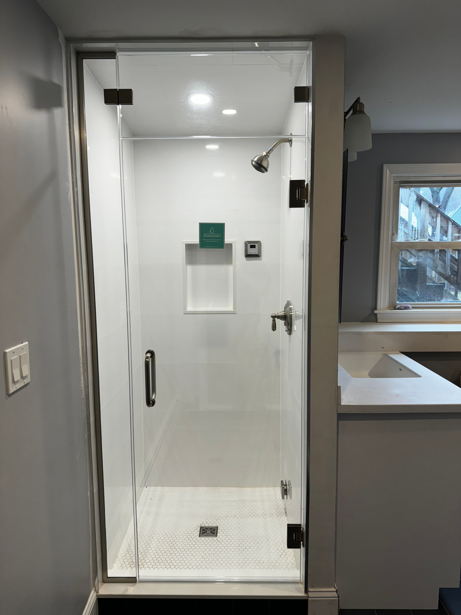 Glass shower with white tile, chrome fixtures, and recessed shelf in a renovated bathroom.