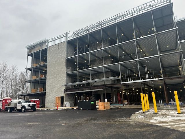 Building under construction with steel framework, grey brick, and a concrete entrance. Cloudy day.