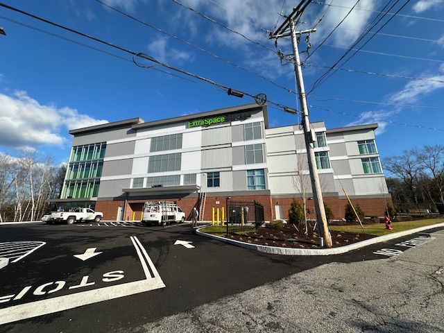 Exterior of a multi-story U-Store-It storage facility with a blue sky. Two white trucks parked in front.