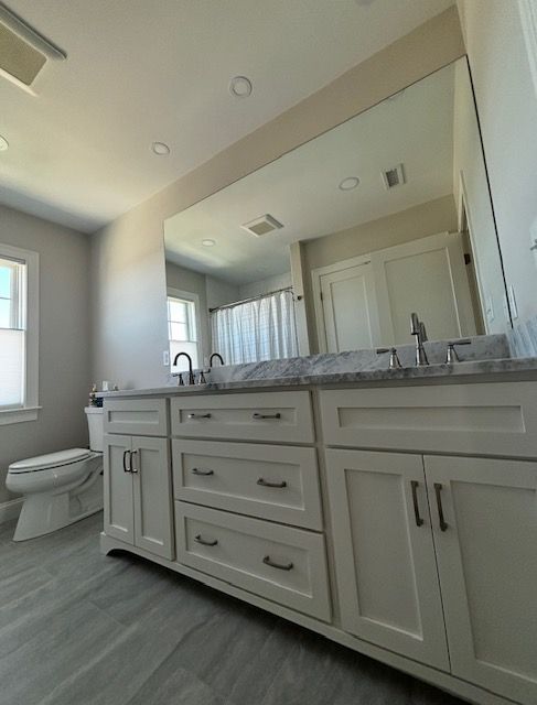 Bathroom with white vanity, large mirror, toilet, and window. Light grey floor and walls.