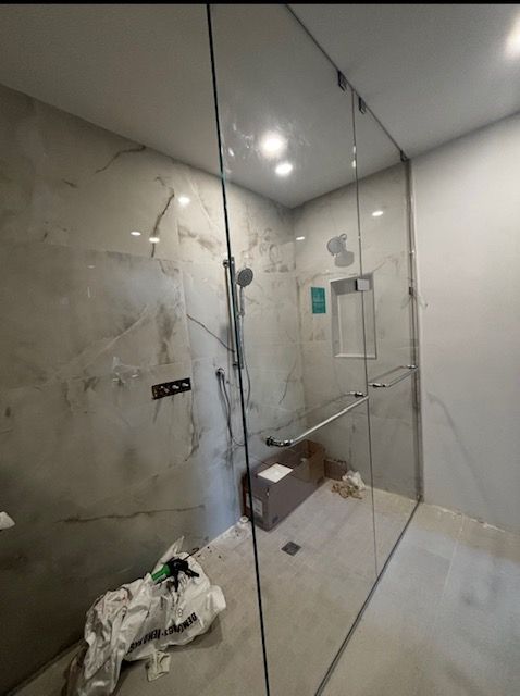 Shower with marble-patterned walls, glass enclosure, and unfinished construction materials.