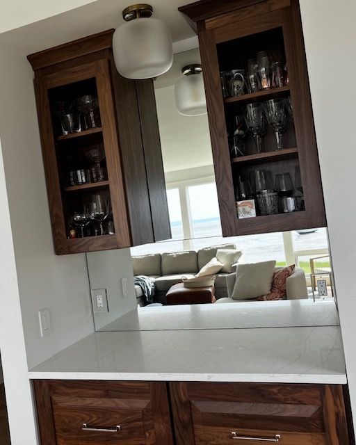 Wooden cabinets with glass doors above a countertop, reflecting a living room with a sofa.