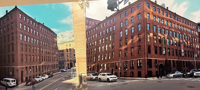 Brick buildings line a city street with parked cars. A bright blue sky is overhead.