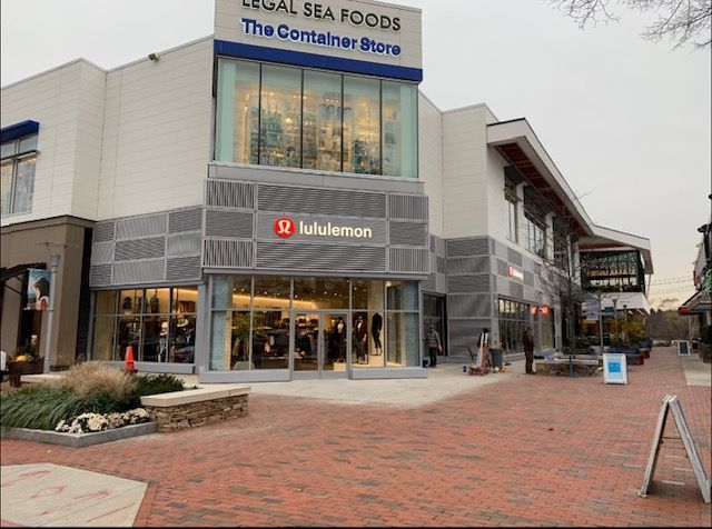 Lululemon store in shopping center with Legal Sea Foods and The Container Store signage. Red brick walkway, clear day.