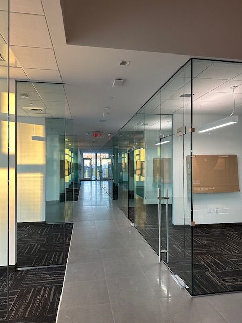 Hallway with glass-walled offices. The hallway has a light gray floor and dark carpeted office areas.