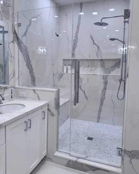 White bathroom with marble walls, glass shower enclosure, and vanity.