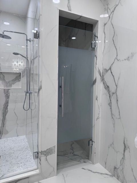 Modern bathroom with glass shower door, marble walls, and silver shower fixtures.