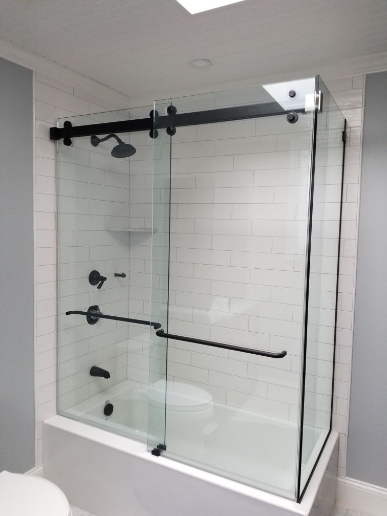 Black-framed glass shower enclosure over a white tub, with black fixtures. White subway tile walls.