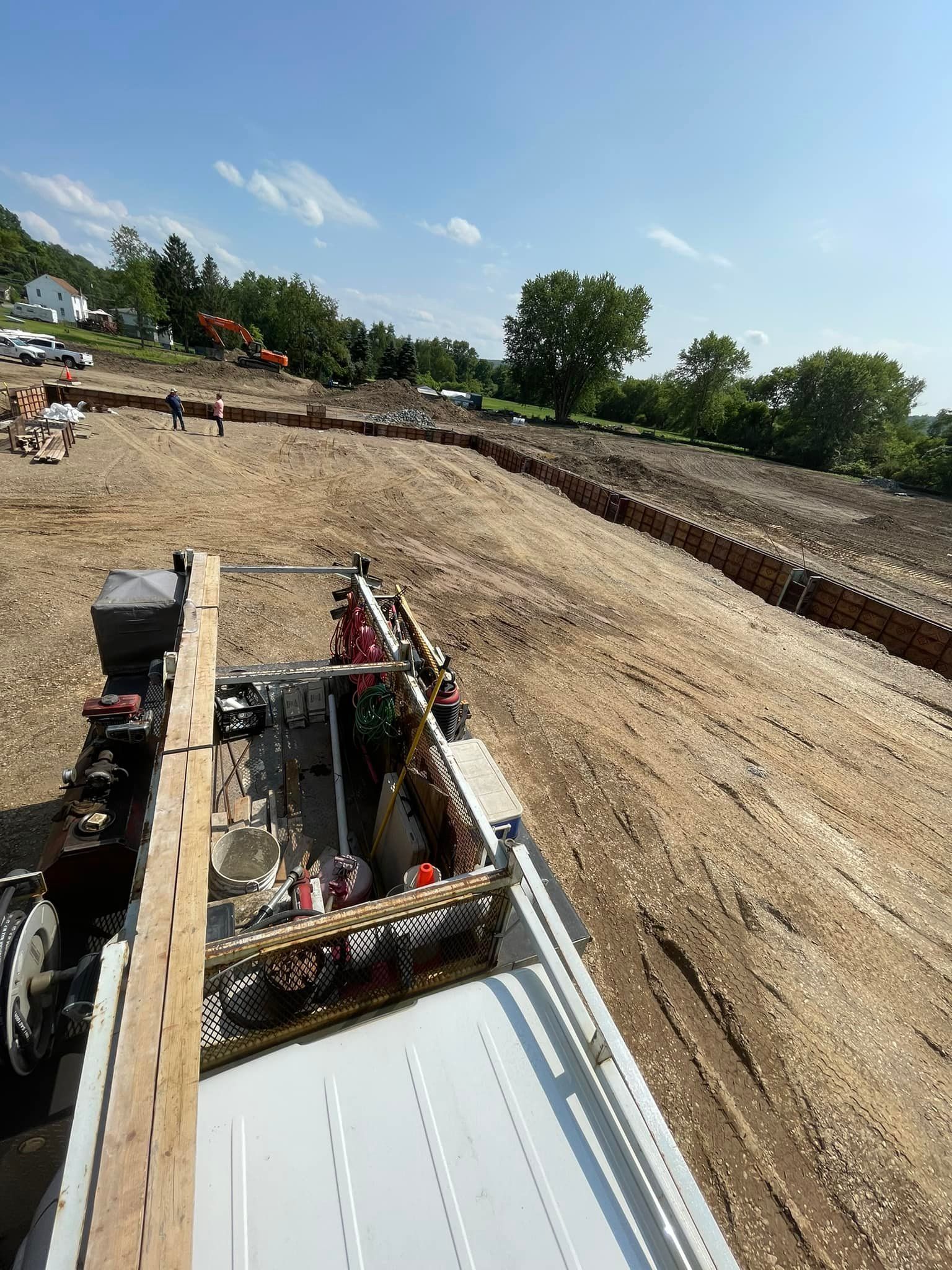 View from the bed of a truck overlooking a construction site with a long, stone retaining wall stretching across a field.