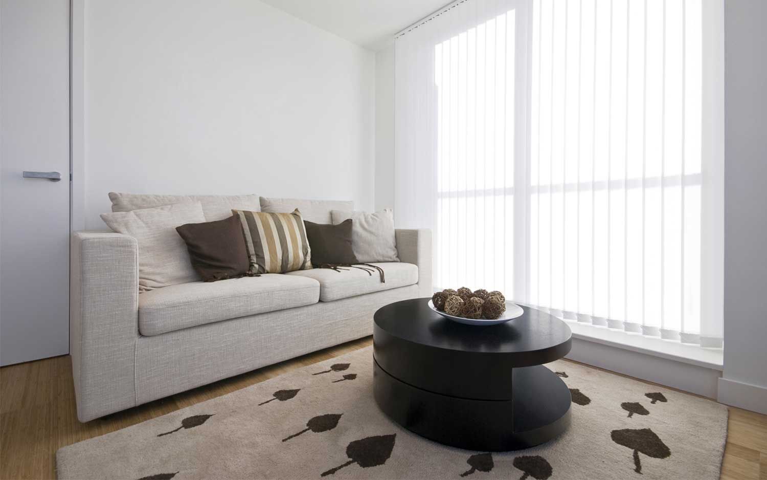 Living room with a beige sofa, dark coffee table, and large window with sheer curtains.