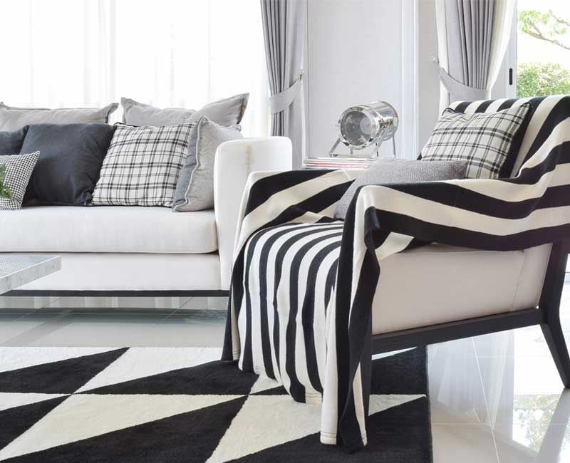 Living room with white sofa, black and white striped blanket on chair, patterned rug.